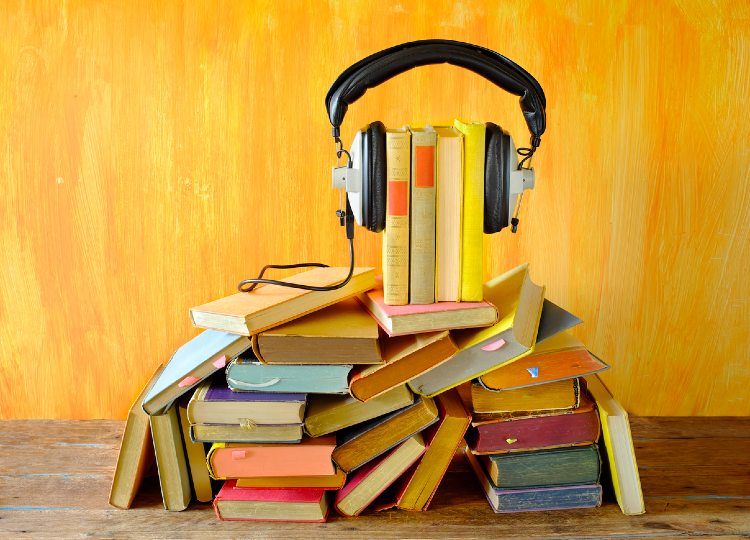 Mehrere Bücher sind übereinander gestapelt. Kopfhörer sind an den Büchern angebracht.