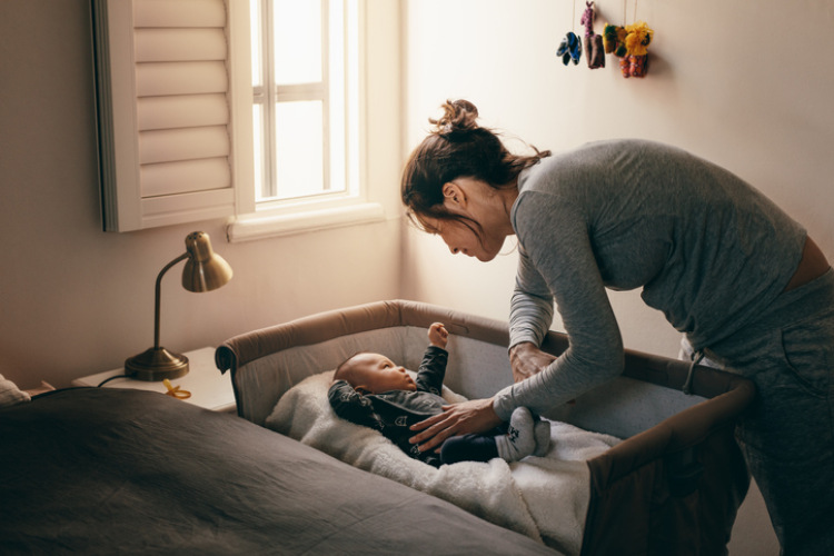 Mutter die Ihr Kind ins Babybett legt