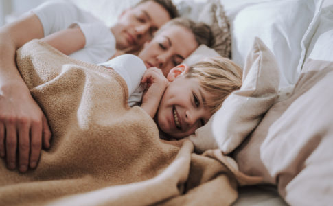 Kind liegt glücklich im Bett mit seinen Eltern