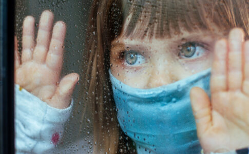 Kind am Fenster mit Maske