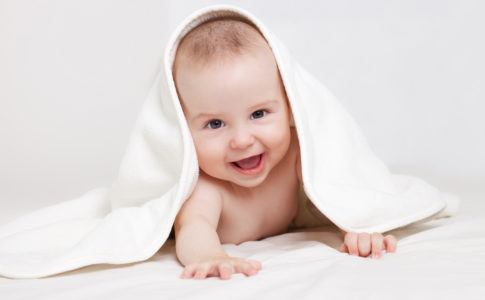 Ein fröhliches Baby unter einer weißen Decke