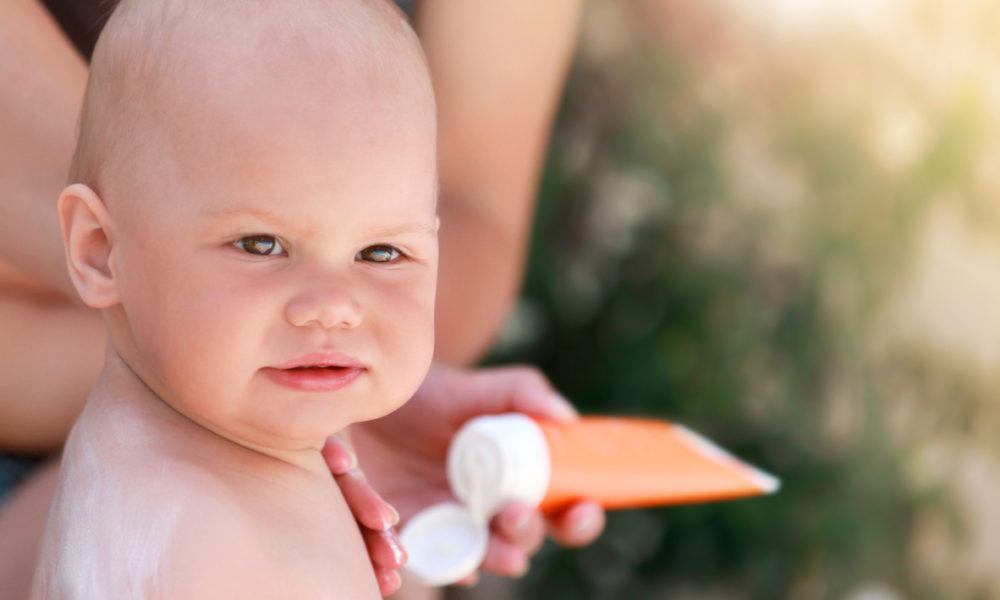 Ein Kleinkind wird von seiner Mutter mit Sonnenschutzcreme eingecremt