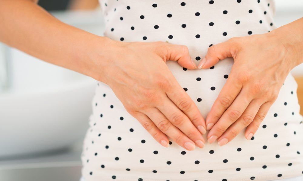 Schwangere Frau hält ihre Hände in Herzform vor ihren Bauch