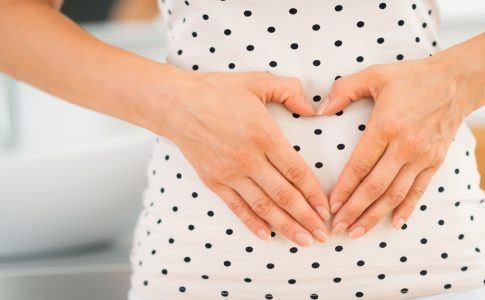 Schwangere Frau hält ihre Hände in Herzform vor ihren Bauch