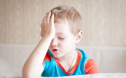 Kleiner Junge hält sich vor Kopfschmerzen den Kopf