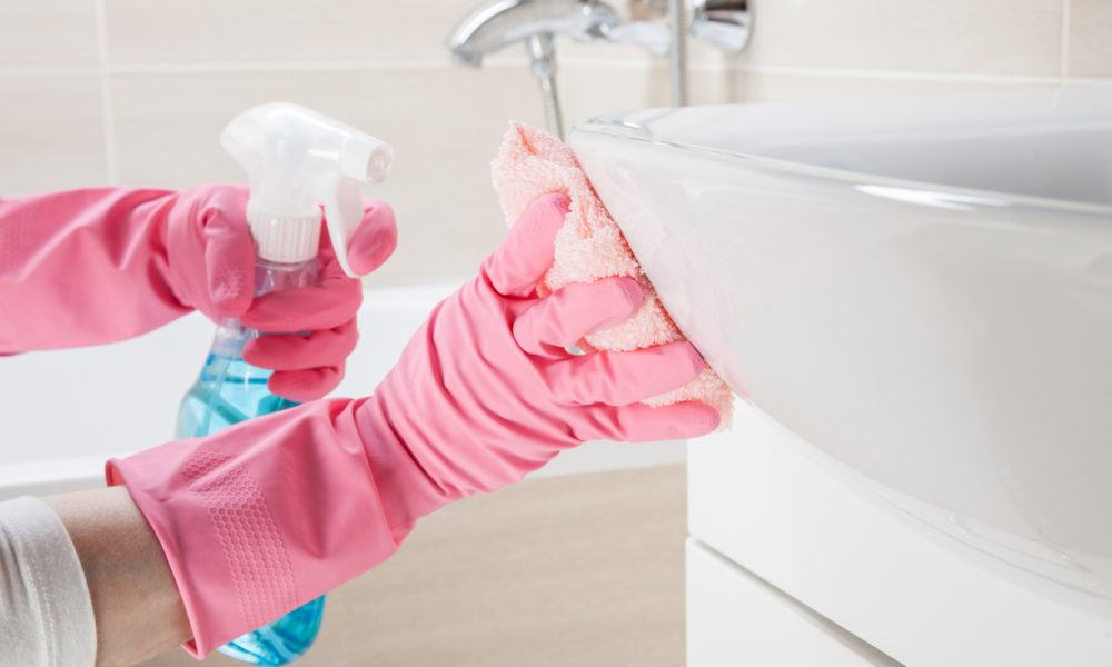 Frau mit Gummihandschuhen putzt das Waschbecken