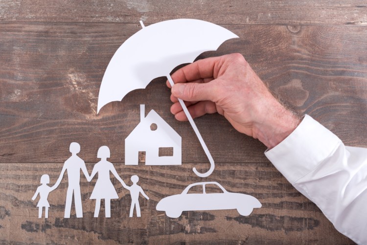 Schirm aus Papier welches eine Familie, ein Haus und ein Auto schützen soll.
