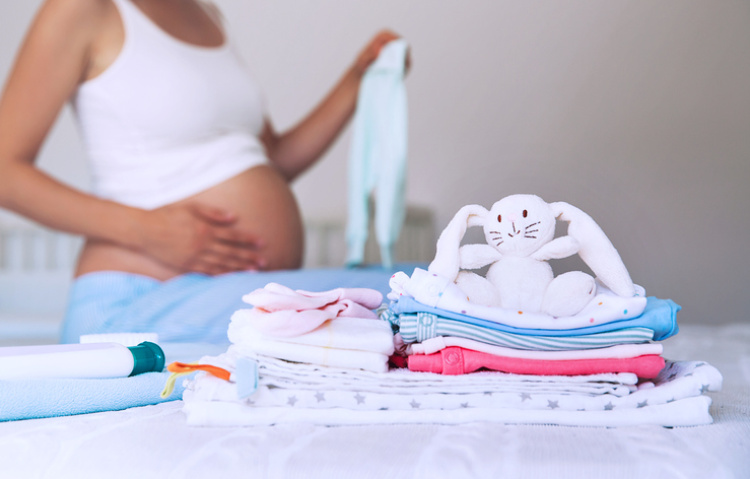 Schwangere Frau steht vor Baby Erstausstattung