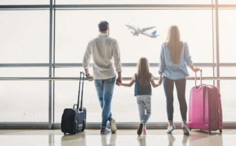 Familie steht am Flughafen vor dem Fenster und schaut sich ein fliegendes Flugzeug an