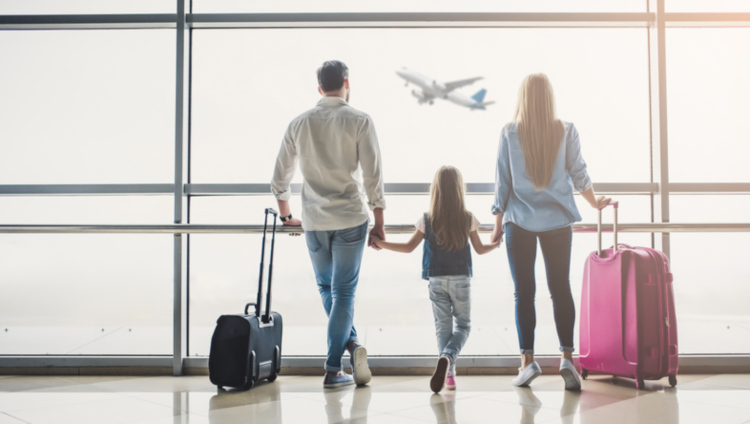 Familie steht am Flughafen vor dem Fenster und schaut sich ein fliegendes Flugzeug an
