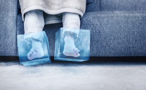 Eine Person mit Eisblöcken an den Füßen sitzt auf einem Sofa.