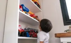 Kind greift nach Spielzeugautos im weißen Regal