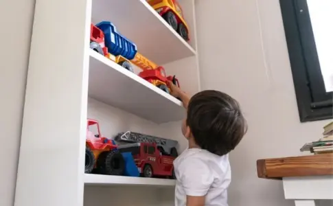 Kind greift nach Spielzeugautos im weißen Regal