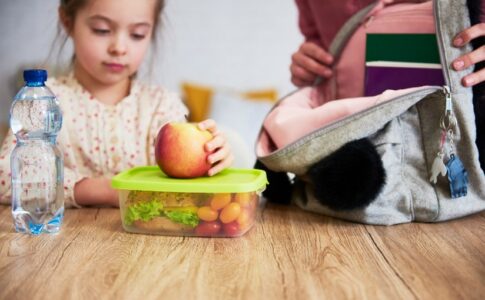 Ein junges Mädchen sitzt am Tisch, vor ihr eine Brotdose