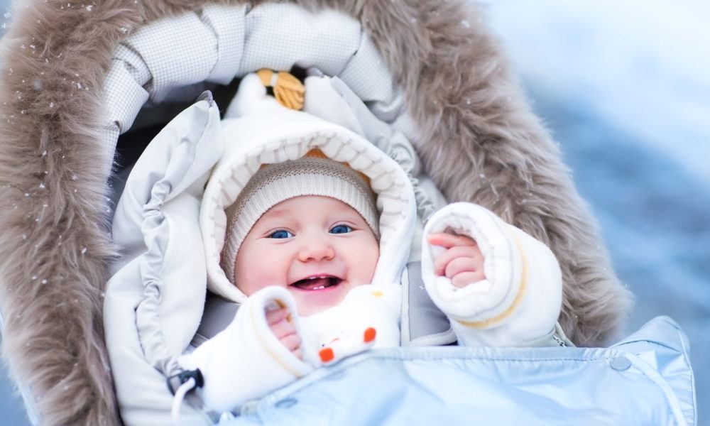 Baby sitzt im Winter warm eingepackt im Kinderwagen und lacht