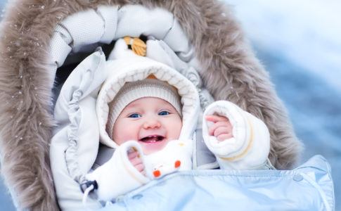 Baby sitzt im Winter warm eingepackt im Kinderwagen und lacht