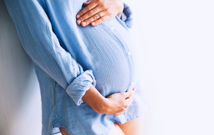 Eine Frau berührt ihren Schwangerschaftsbauch mit der Hand
