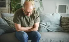 Mann mit Bauchschmerzen auf dem Sofa, mögliche Symptome von Prostata-Problemen