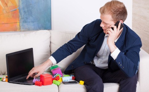 Geschäftsmann sitzt mit Laptop zwischen Spielzeug