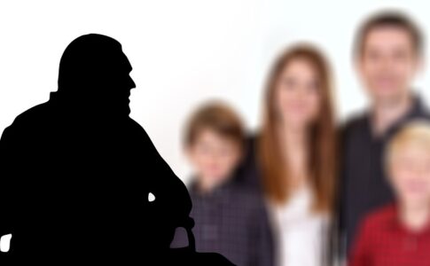 Schwarze Silhouette eines alten Mannes im Rollstuhl, im Hintergrund wird eine Familie mit zwei Kindern gezeigt