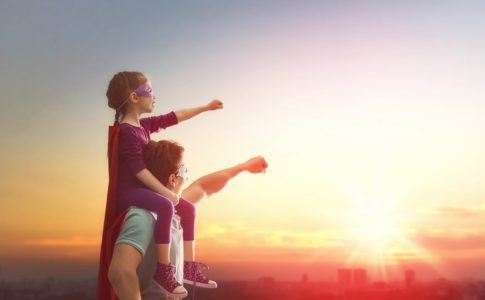Papa trägt Tochter auf Schultern beide im Superhelden Kostüm